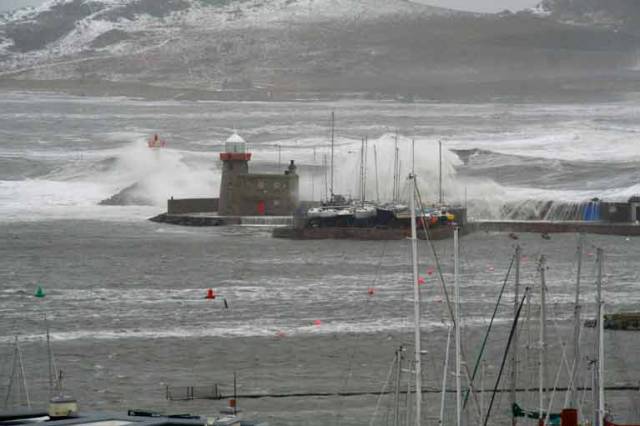 Crazy. Howth Sound at Friday lunchtime, with the East Pier battered at high water at the height of Storm Emma, and the roof of the shed on right sheltering the seven historic Howth 17s beginning to cave in under those monster breakers