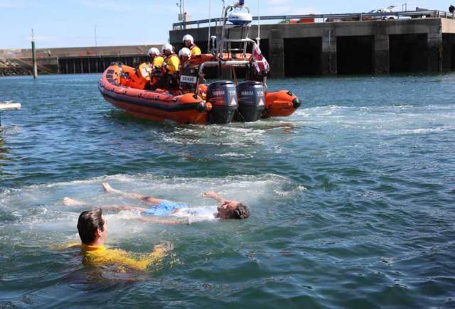 William’s Coates friend Aaron Vance demonstrating the Float to Live survival skill in Bangor marina alongside RNLI lifeguard Charlie Murray, with Bangor RNLI’s inshore lifeboat standing by
