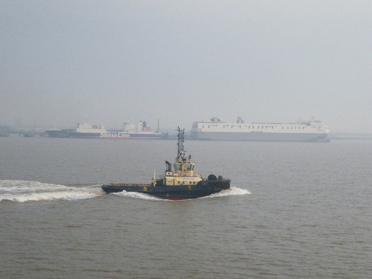 Brexit &#039;Freeports&#039;: Logistics UK welcomes the move to offer ‘an ambitious customs model, measures to speed up planning processes, and a commitment to geographic flexibility and opportunities for all transport modes’. Above AFLOAT&#039;s photo of a hazy Humber Estuary (Killingholme) on the North Sea. On the right Delphine which in 2018 joined sister Celine dubbed the &#039;Brexit-Buster&#039; on Ireland-mainland Europe services of Dublin-Belgium/Netherlands. On the left another ro-ro freight-ferry Stena Scotia currently operates on the Irish Sea between Belfast and Heysham, England. In the foreground heading upriver the 70 bollard pull tonnes tug Svitzer Laura.
