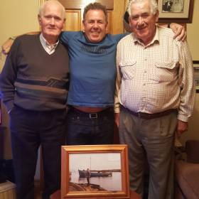 (from left) Michael, Jim and James Gallagher at home in Burtonport, Co Donegal with a photo of half-decker Irine which helped to rescue 15 people, mainly young children, off Roaninish in August 1956