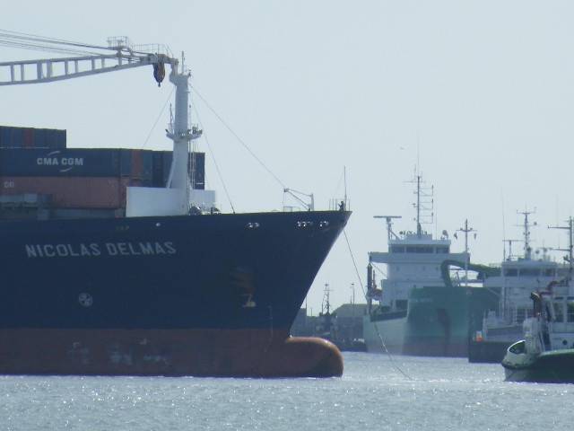 Bow of departing CMA CGM containership Nicolas Delmas in Dublin Port along with vessels berthed on the south bank including an Arklow Shipping 'B' class cargoship been unloaded 